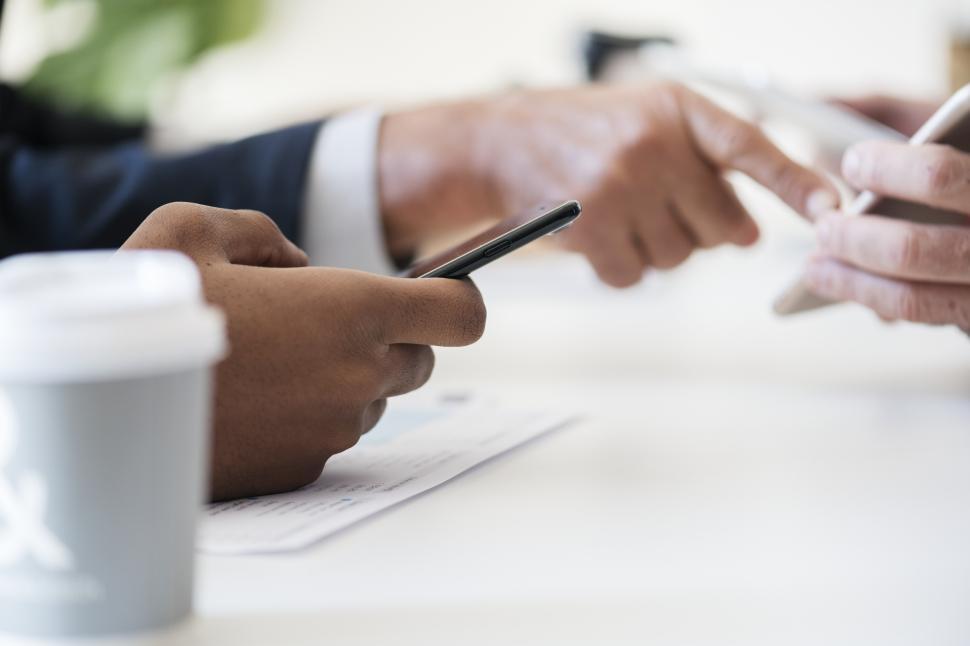 Free Image of Close up of two people holding mobile phones at a community table 