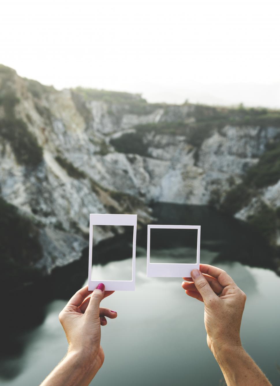 Free Image of Hands holding a photo frame shaped paper cut out templates in front of mountains 