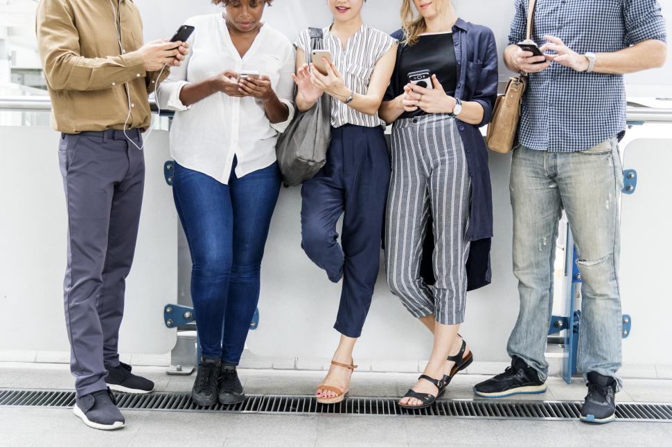 Free Image of Colleagues looking at their mobile phones, leaning on a wall 