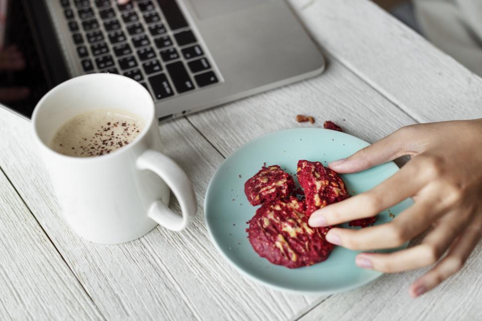 Free Image of Close up of a woman s hand picking red velvet cookie from the plate 
