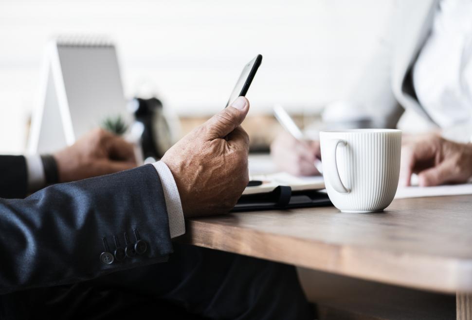 Free Image of Close up of person holding a mobile phone at a desk 