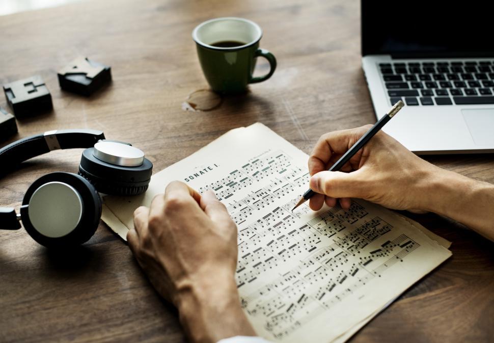 Free Image of Overhead view of a person s hand writing musical notes on a sheet of paper 