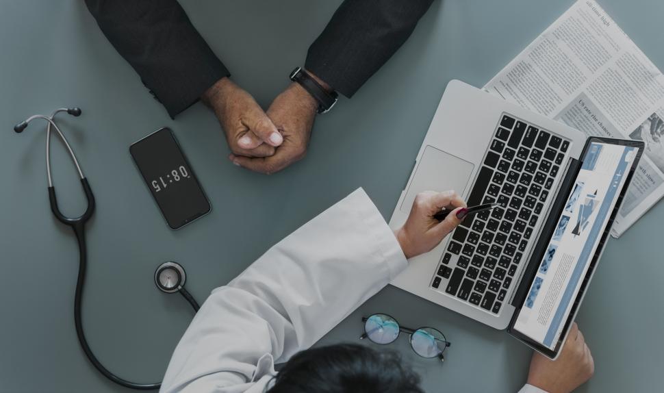 Free Image of Overhead view of a doctor pointing at the laptop screen with a pen 