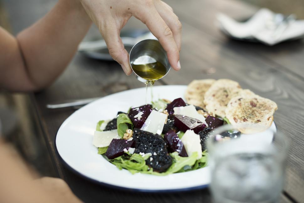 Free Image of Close up of a hand pouring olive oil on a salad 