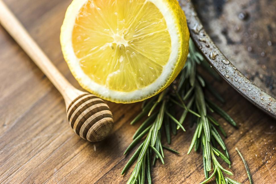 Free Image of Close up of a lemon cut in half, rosemary leaves and a honey dripper 