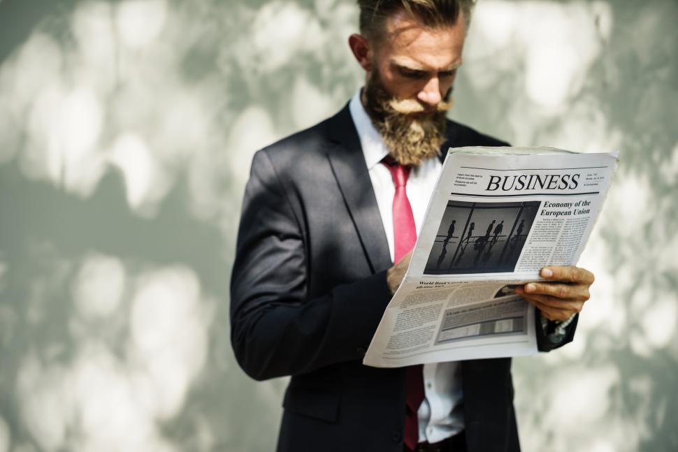 Free Image of A bearded man standing outdoors reading a newspaper 