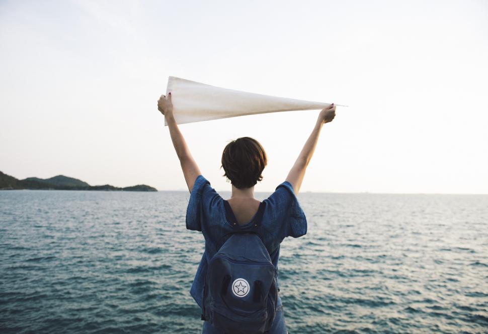 Free Image of A young Caucasian woman holding white flag high at a seashore 