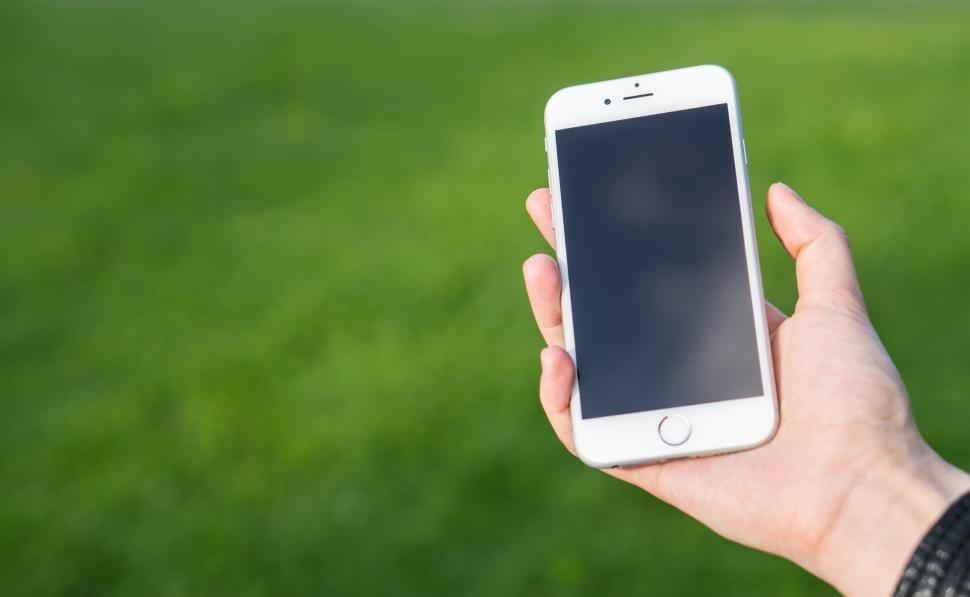 Free Image of A hand posing with a smartphone over green grass 