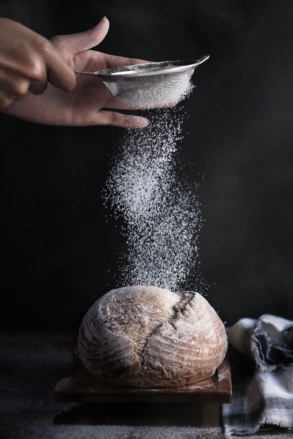 Free Image of Baker sprinkles powdered flour on bread 