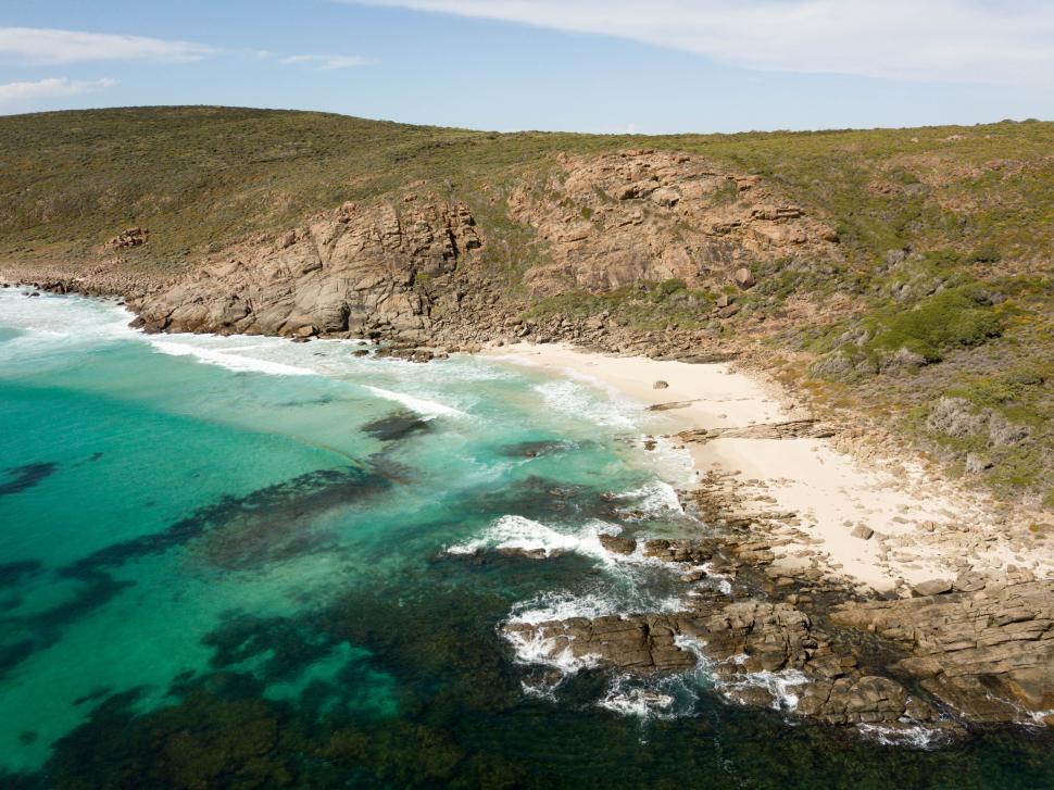 Free Image of Aerial view of ocean waves with hills on an empty beach.  