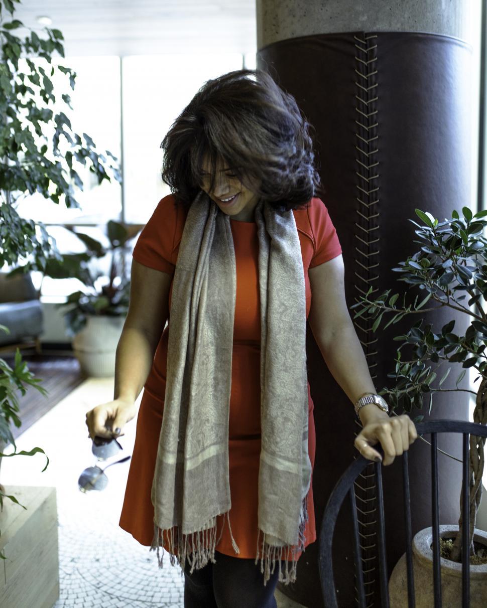 Free Image of Young Woman in grey scarf standing and holding sunglasses in hand in a restaurant 