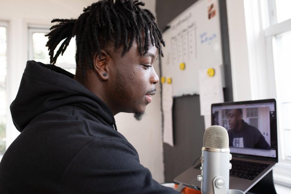 Free Image of Young Male Vlogger using mic with laptop in the background 