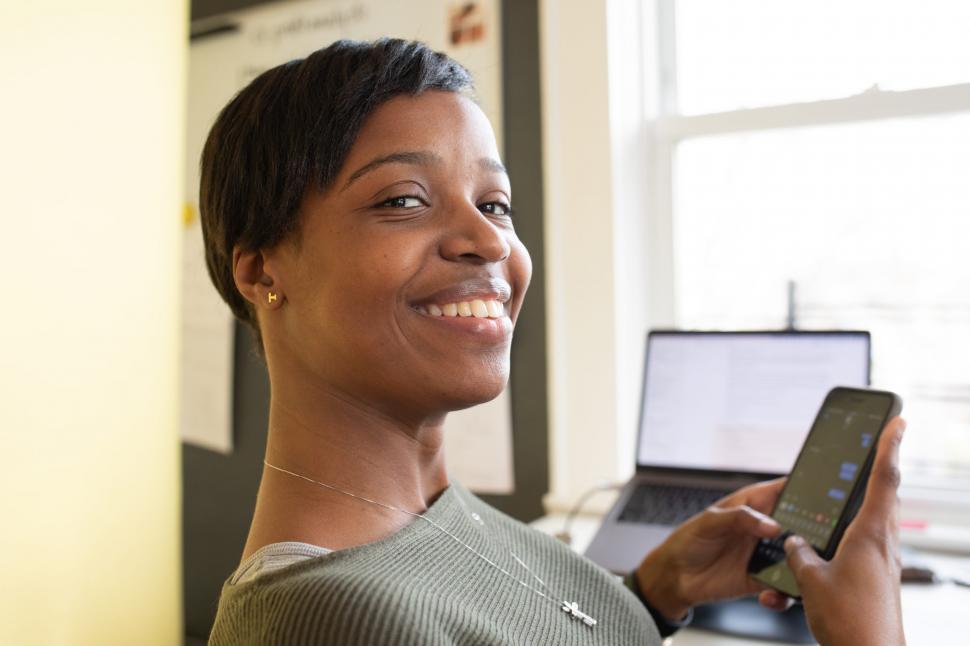 Free Image of Young Smiling Woman Typing on Mobile Phone in Office - Looking a 