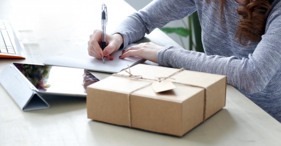Free Image of Package on the desk, woman writing on the card 