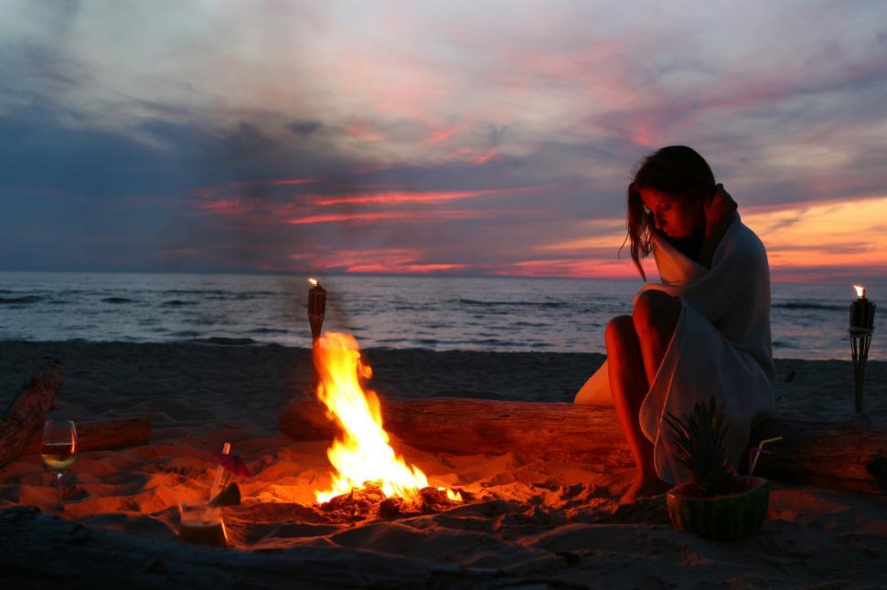 Free Image of Young woman sitting by fire at the beach 