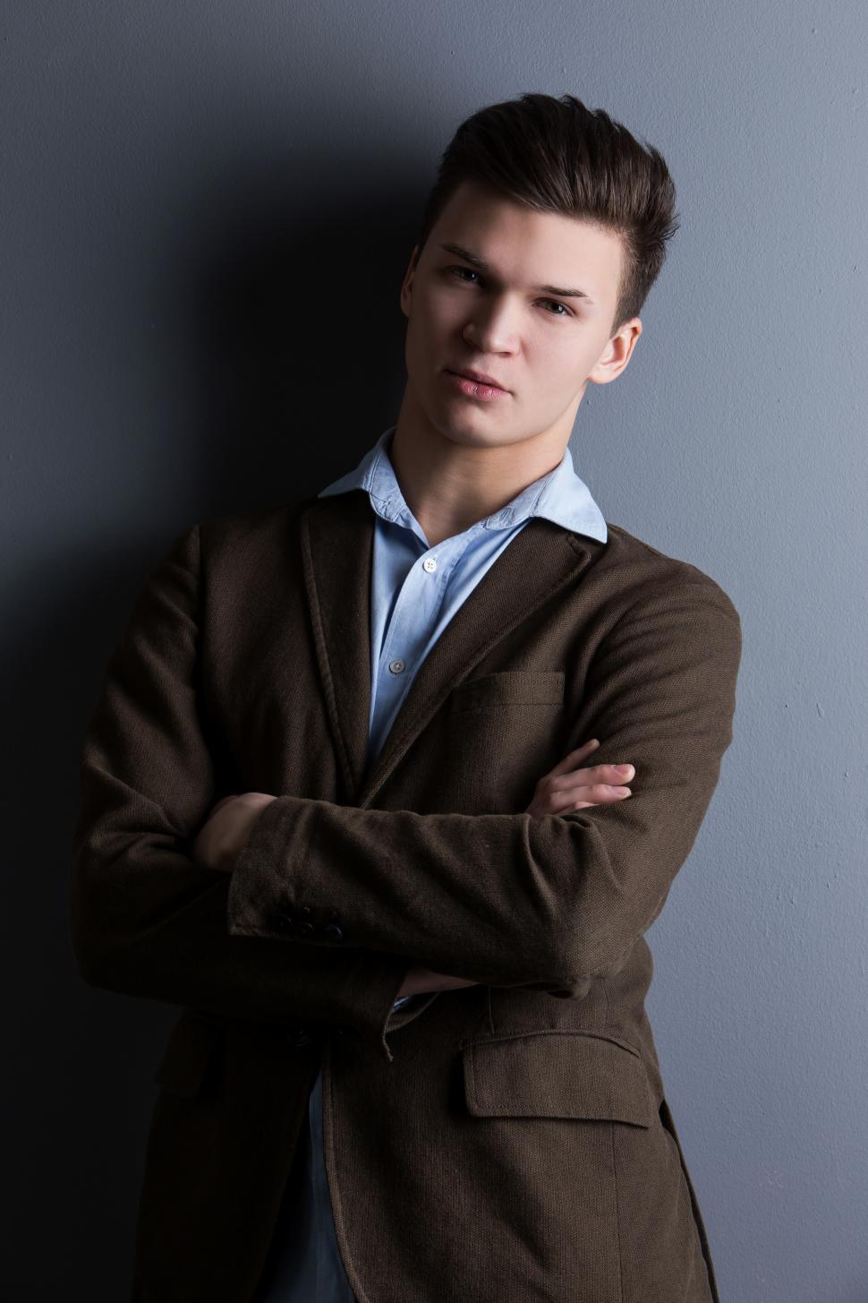 Free Image of Well-dressed man with arms crossed, leaning on wall 