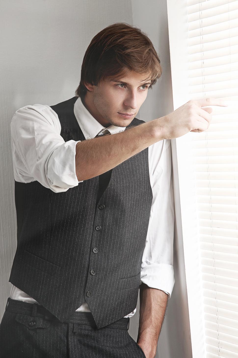 Free Image of Man in dark vest peering through the blinds 