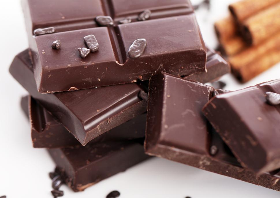 Free Image of Pieces of chocolate with background cinnamon sticks 