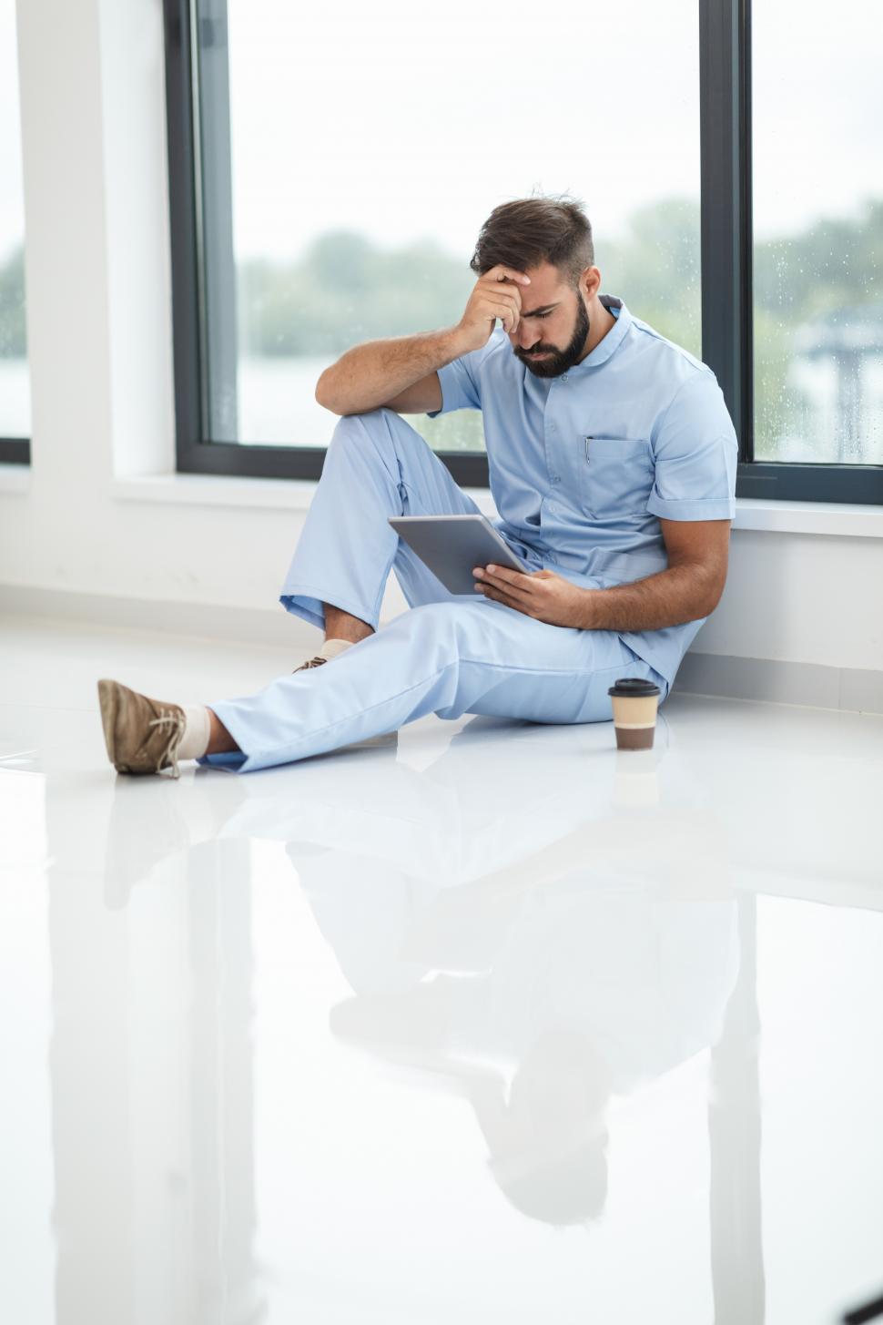 Free Image of Male nurse with upset expression sitting on the ground - hand on 