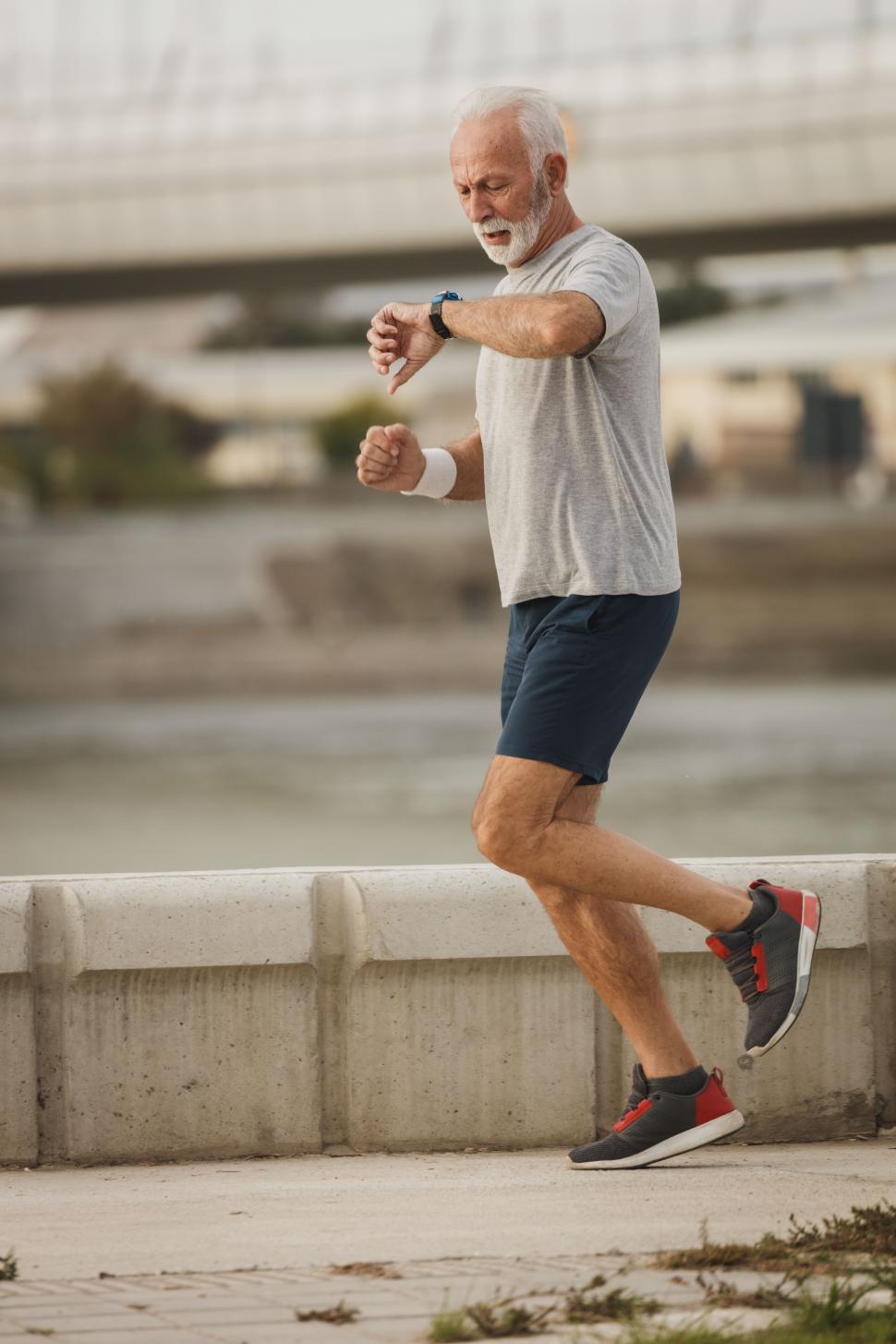 Free Image of Senior man looking at his wristwatch while running on the bridge 