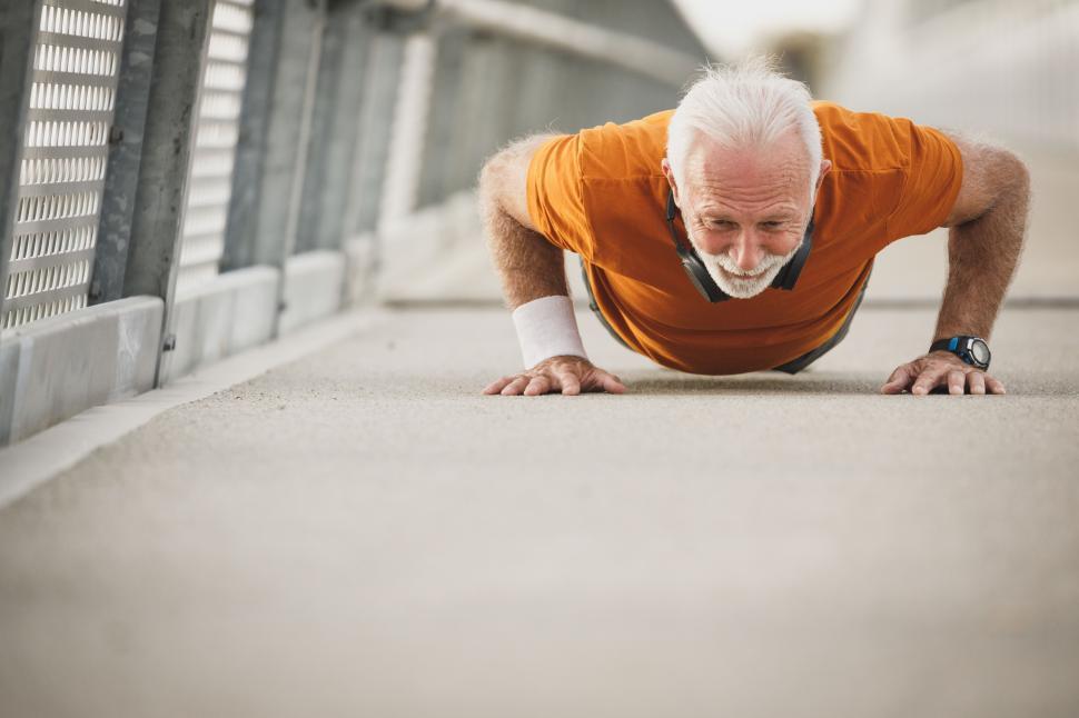 Free Image of Senior man with headphones on neck doing push-ups 