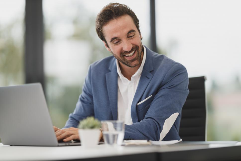 Free Image of Happy office worker working on a laptop with paper notes 