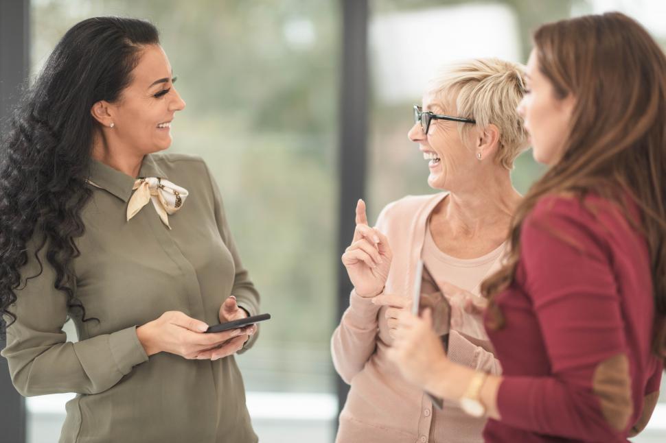 Free Image of Three female co-workers energetically talking while standing in the office 