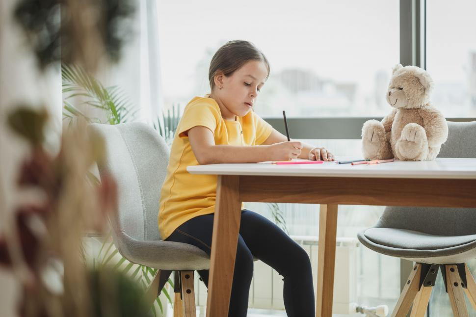 Free Image of Little girl doing homework with a teddy bear 