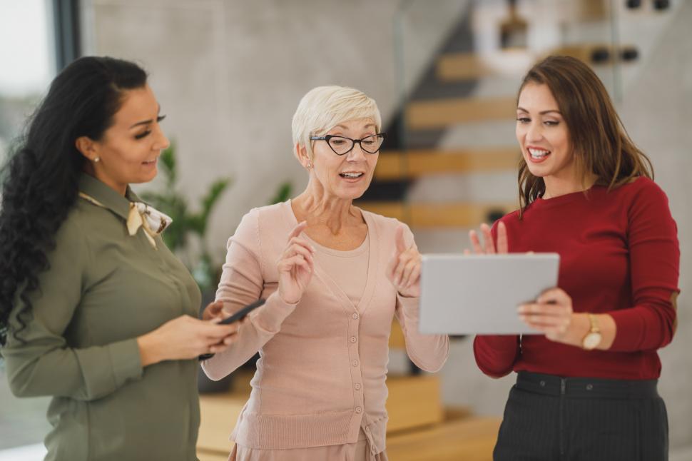 Free Image of Three female coworkers talking and smiling while standing in the workplace 