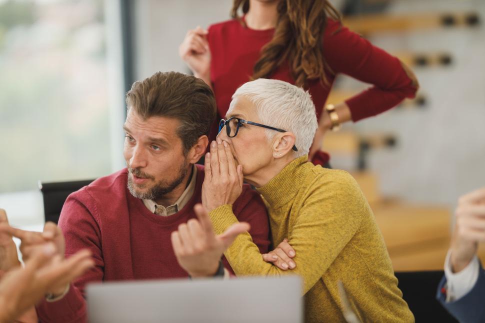 Free Image of Female coworker whispering in the ear of her young male team member 