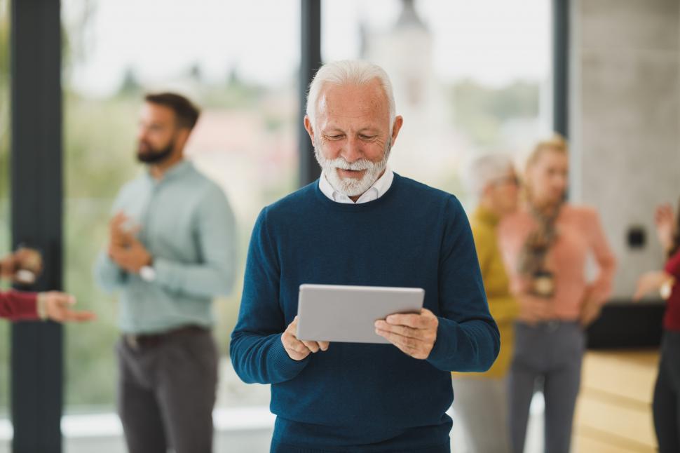 Free Image of Senior male executive smiling while reading with tablet in office 