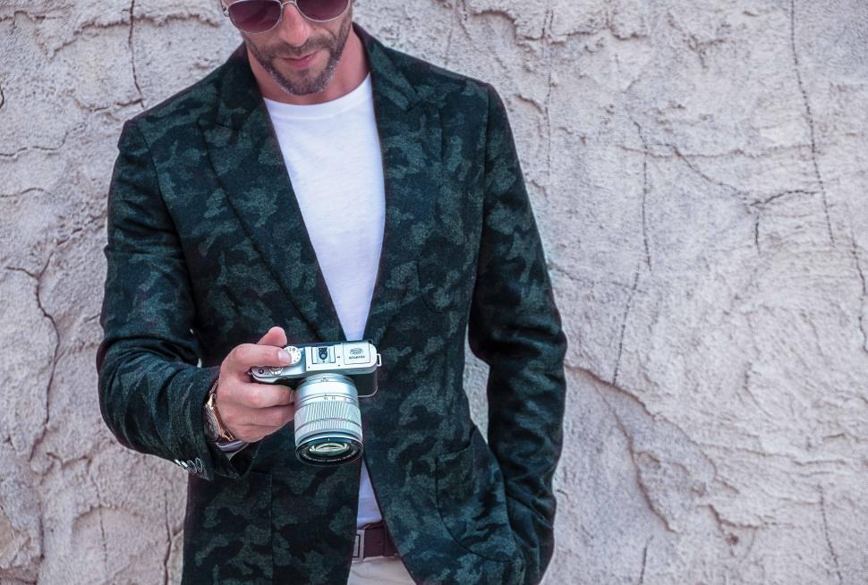 Free Image of Man in suit with camera standing against cracked wall 