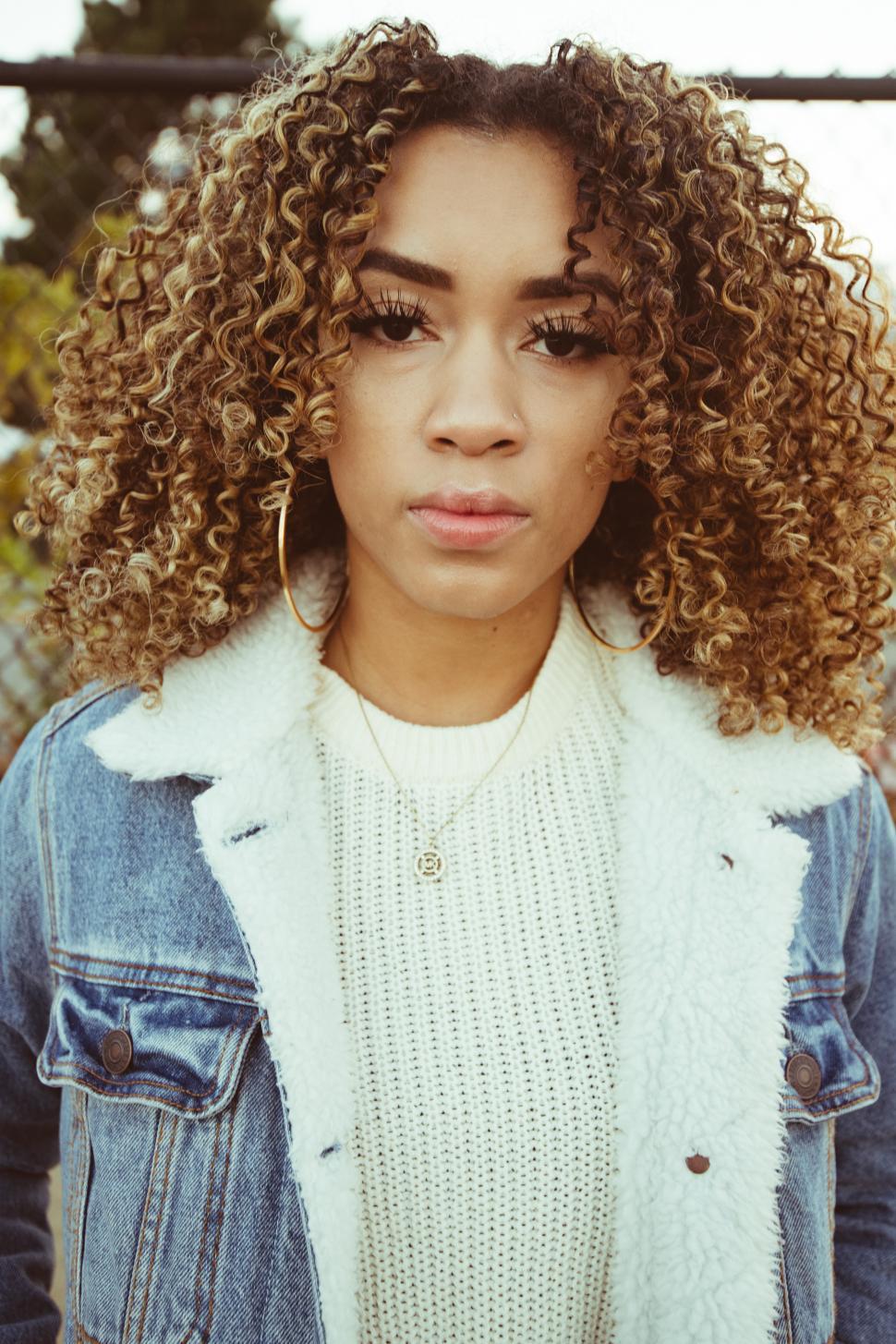 Free Image of Young woman in white sweater and hoop earrings posing for camera 