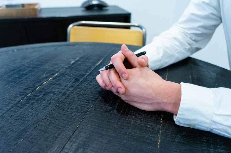 Free Image of Folded hands and pen on table 