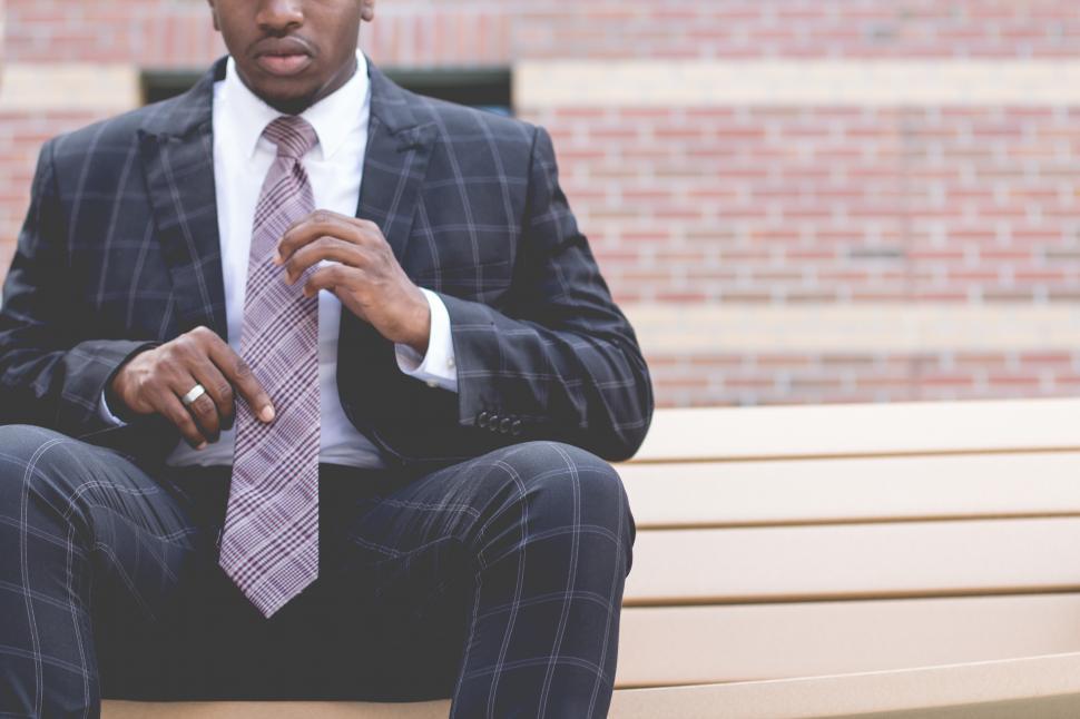 Free Image of Young man in blue chequered suit, sitting outside a building 
