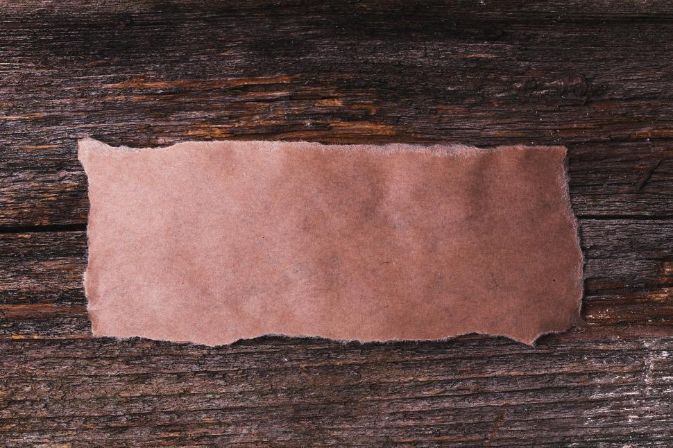 Free Image of Blank rectangle of torn paper on rough wooden background 