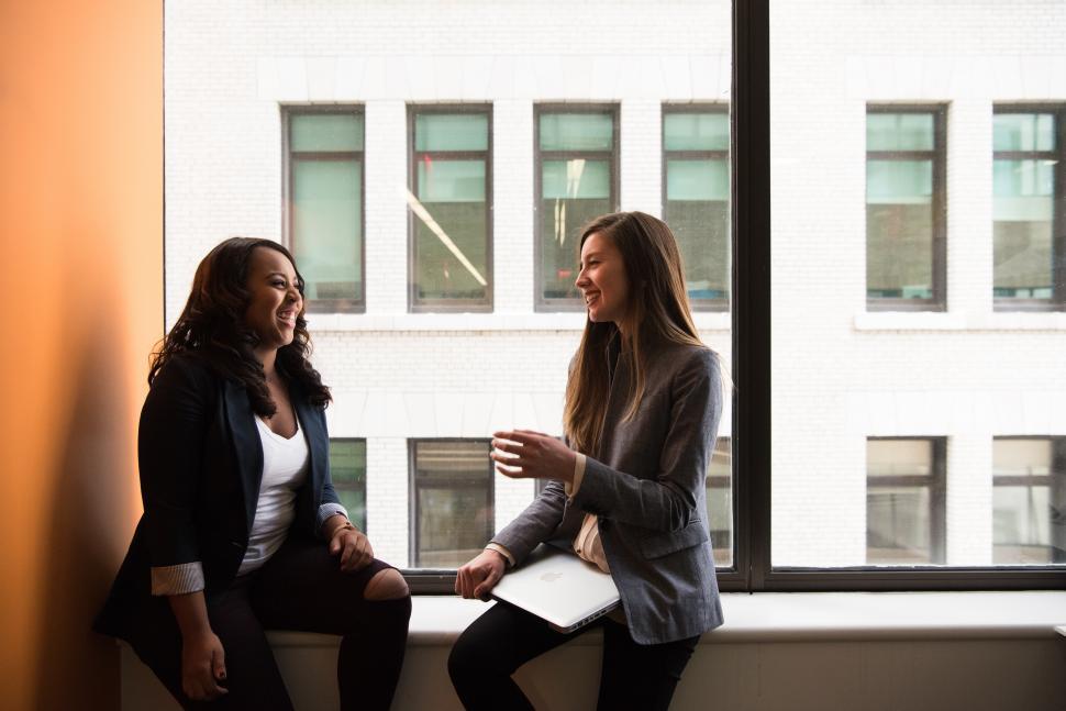 Free Image of Happy Businesswomen talking to each other near glass window 