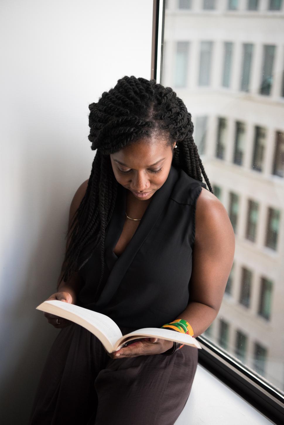 Free Image of Woman reading book near glass window - looking down 