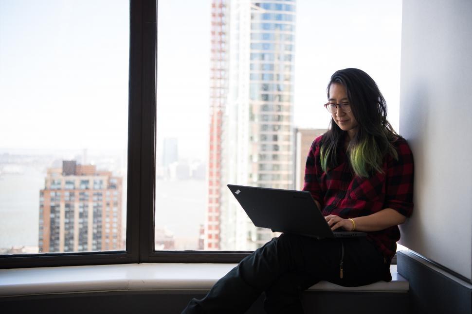 Free Image of Female executive in glasses working on laptop near glass window 