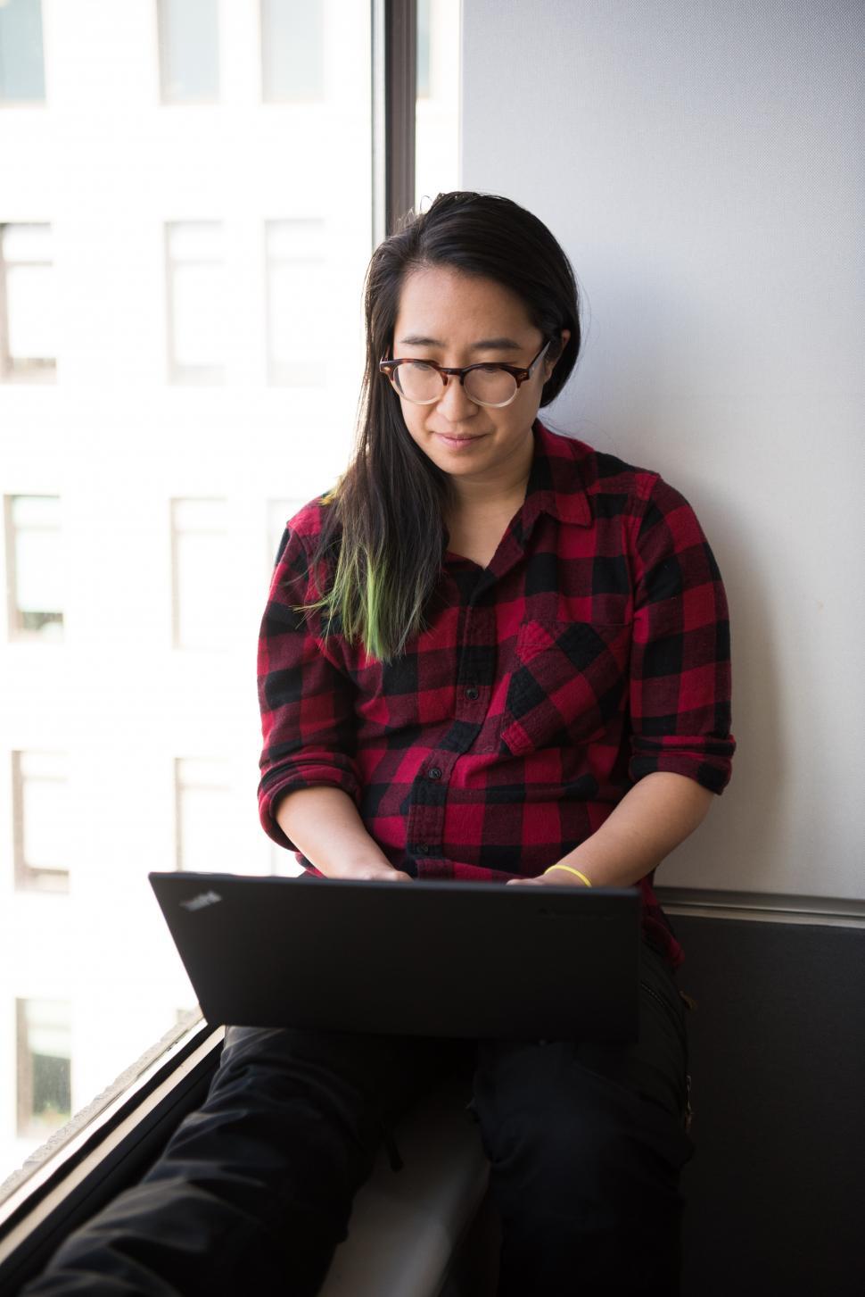 Free Image of Female executive in glasses using laptop near glass window 