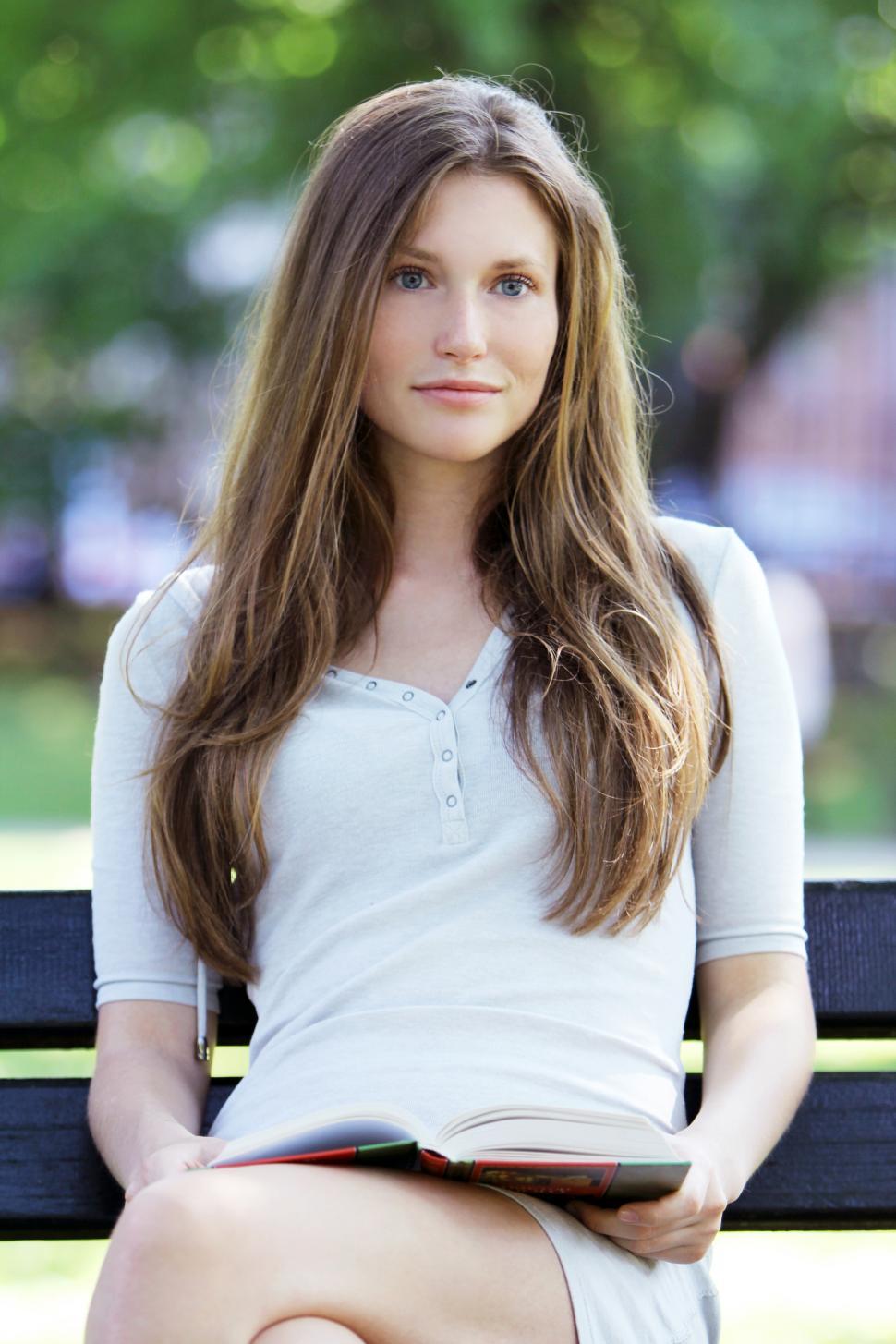 Free Image of Young woman on a bench reading book in the park 