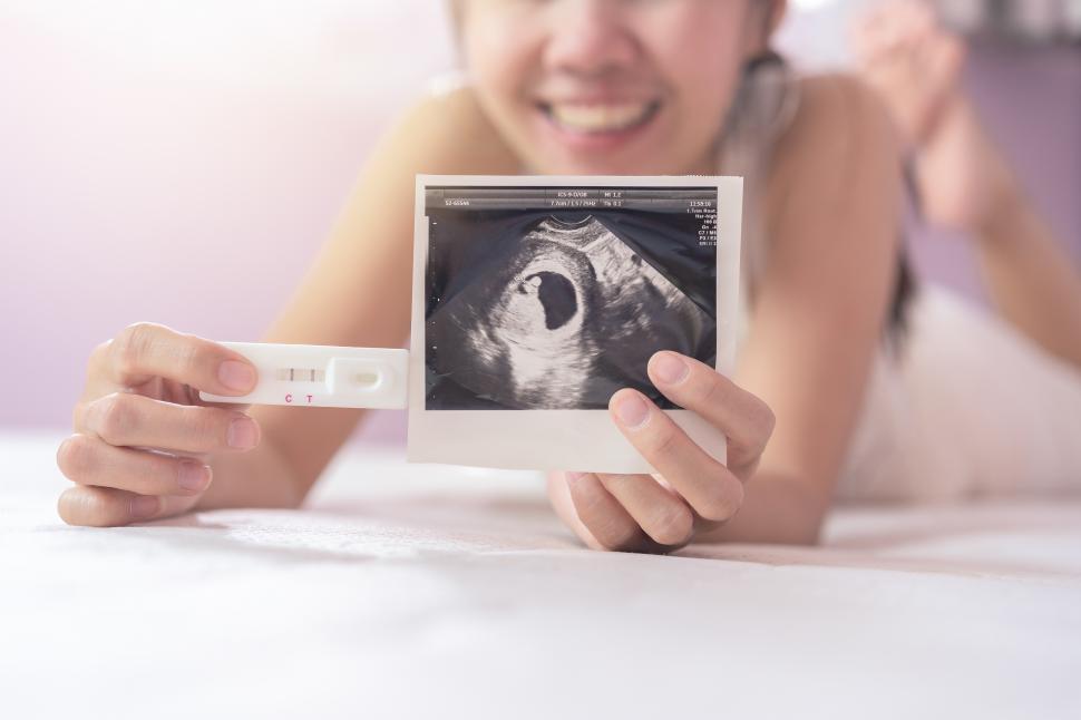 Free Image of Pregnant asian woman in white dress hole and show a pregnancy test 