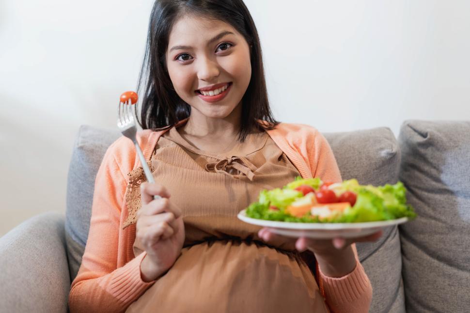 Free Image of Happy pregnant Asian woman sitting and eating natural food 