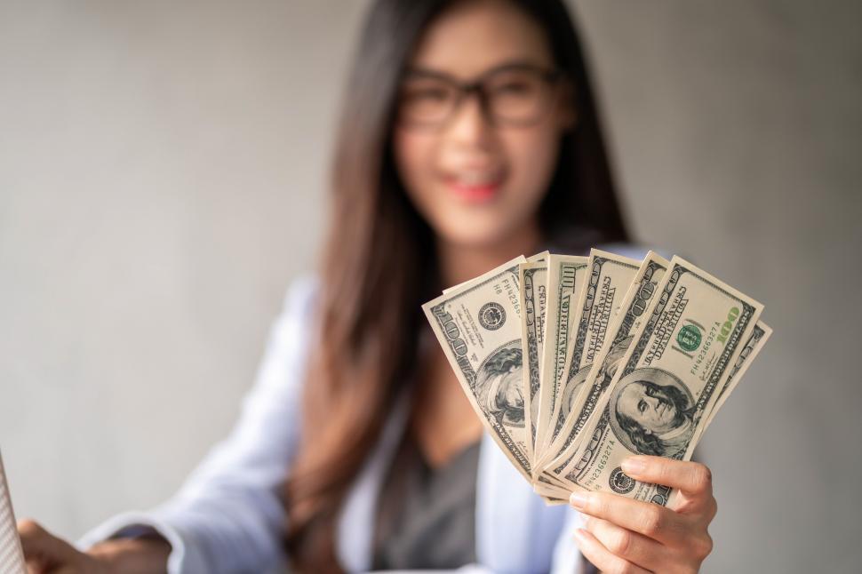 Free Image of Dollar in a businesswoman hand. An Asian woman is working from home. 