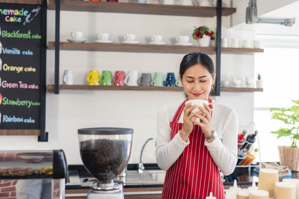 Free Image of Woman owner standing at her coffee shop gate holding hot coffee 