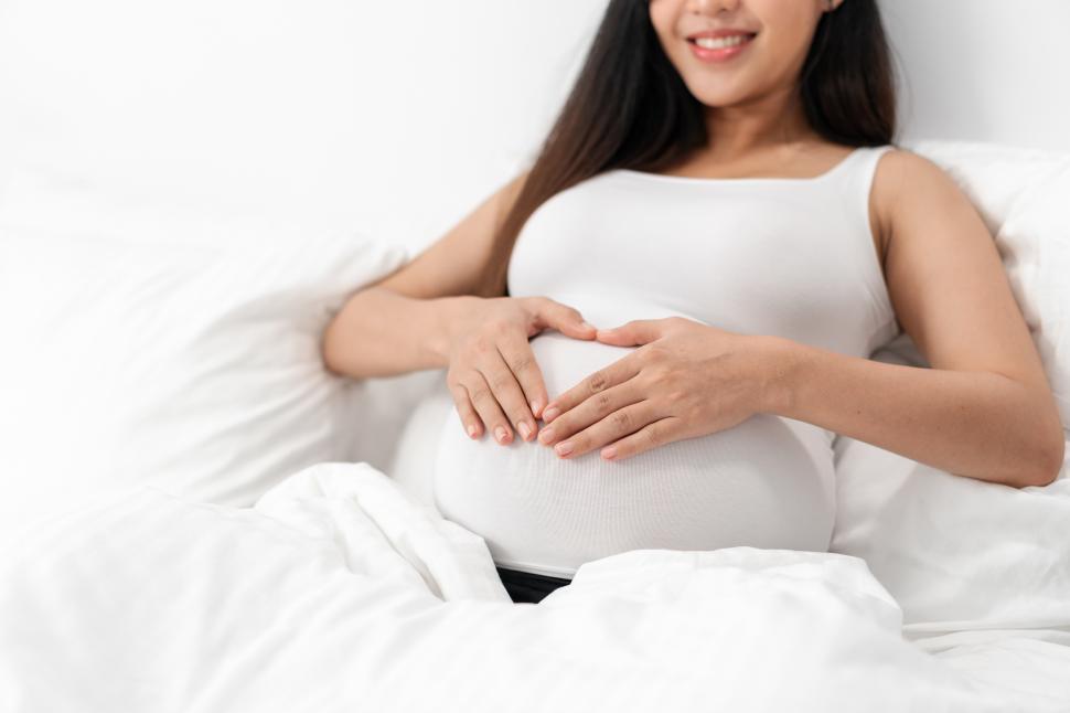 Free Image of Happy pregnant woman is sitting on bed 