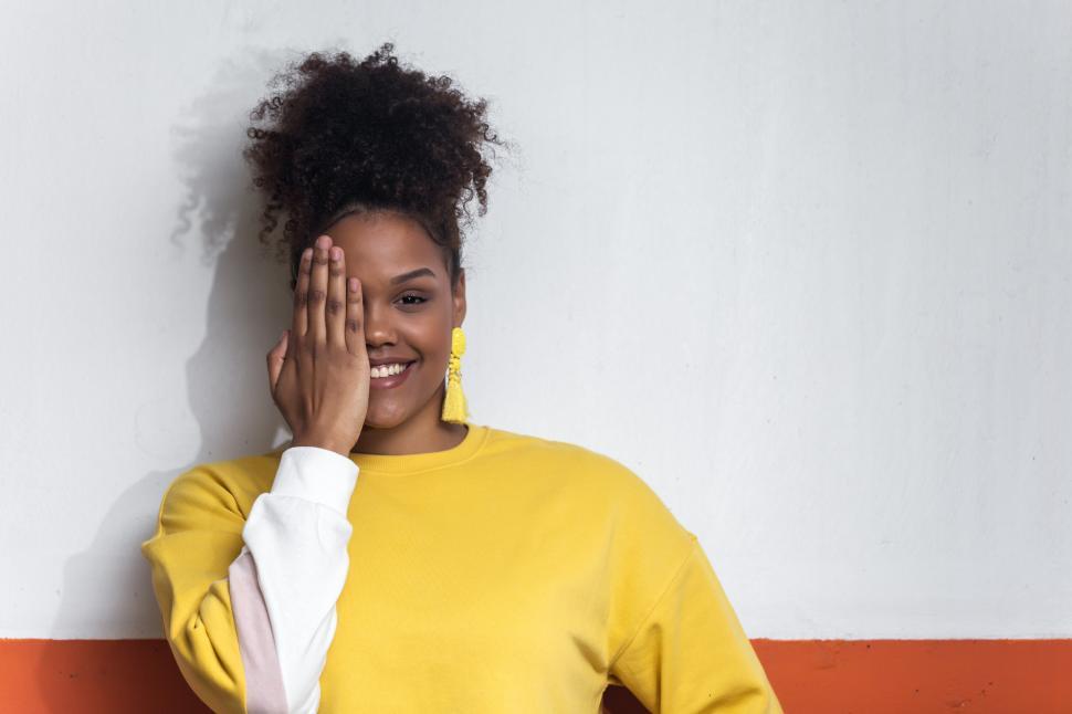Free Image of Smiling black woman in yellow outfit covering eye with hand 