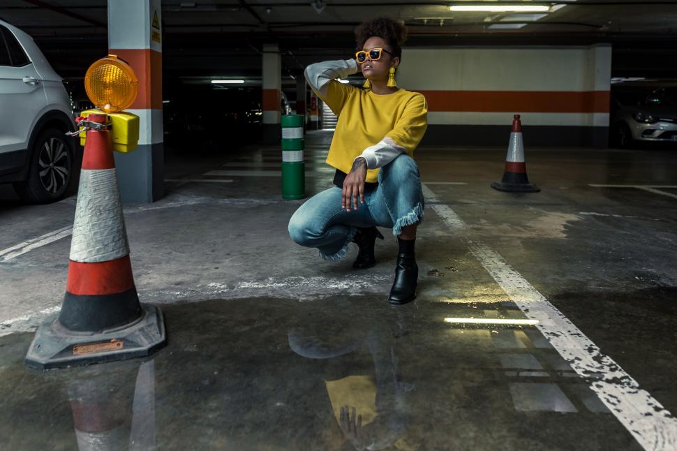 Free Image of Stylish ethnic woman kneeling in parking lot 