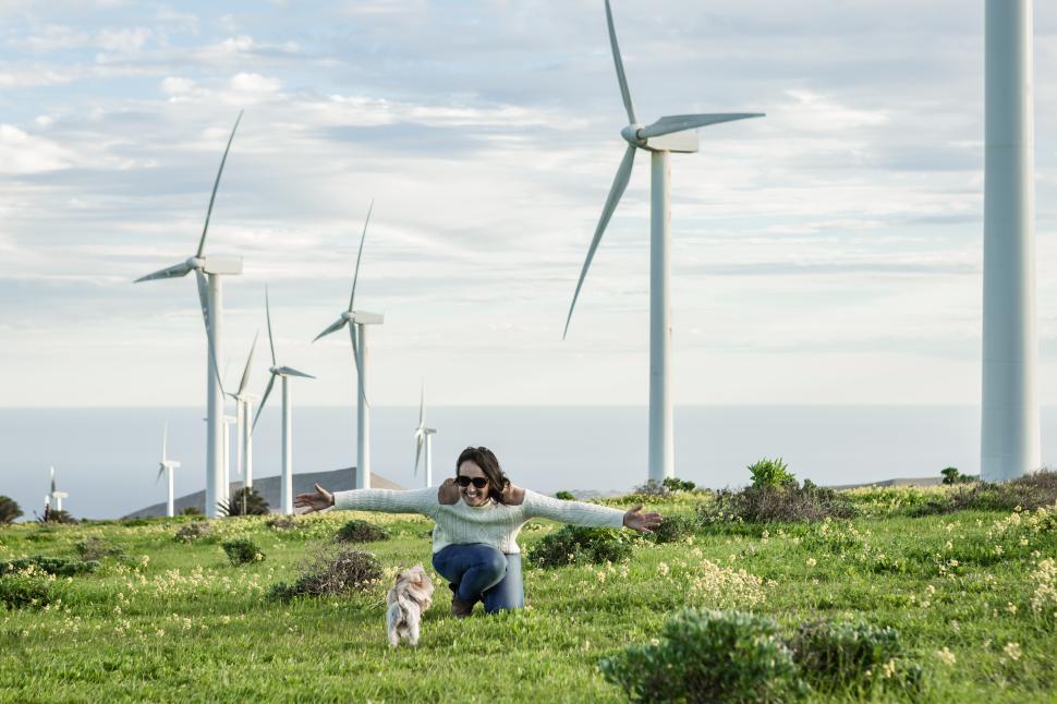 Free Image of Smiling woman playing with dog in meadow with windmills 