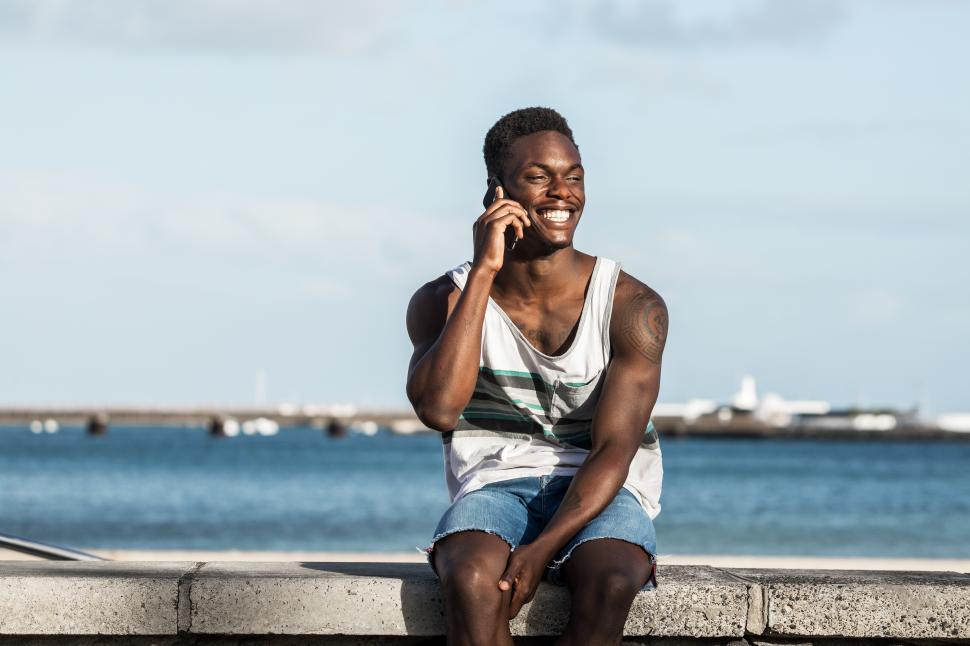 Free Image of Positive black man speaking on smartphone at seafront in summer 